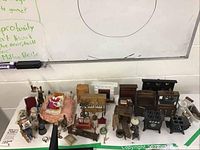 Full view of all dollhouse furniture and figurines arranged on a table, showing wooden furniture including beds, chairs, and cabinetry, with figurines and small accessories.