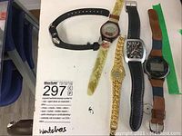 Top view of all 5 watches laid out: black rubber strap, translucent dinosaur-themed strap, gold-tone bracelet watch, black leather strap watch, black digital watch with brown leather strap