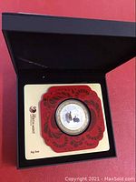 Silver coin displayed in original black box with red decorative holder.