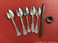 Photo of five ornate sterling silver tea spoons with a part of a metal comb and a metal ring on a red background