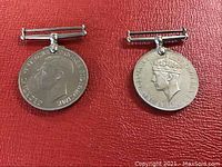 View of two sterling silver World War medals laid on red background, showing front profiles of King George VI and King George V