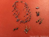 Full lot layout showing fresh water grey pearl multi-strand necklace and five pairs of earrings on textured red background