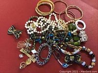 Multiple assorted costume jewelry pieces including bracelets, necklaces, hair clips, and rings shown on a red surface.