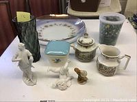 Overall lot view showing all items on table including figurines, vase, jar of marbles, glass platters, sugar and cream set, and Meakin bowl.