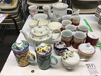 Photo showing full collection of teapot, coffee mugs, cups with saucers, lidded bowls, and teacups arranged on table.