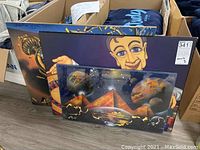 Box with three prints: two mounted with cosmic pyramid artwork and cartoon human character, one sealed.