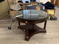 Full view of round table showing green marble top, wood base with gold accents, placed on hardwood floor surrounded by miscellaneous items.