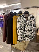 Four men's jackets on hangers including black and white floral blazer, mustard yellow, maroon, and dark colored jackets