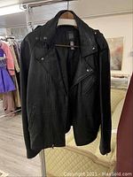 Black leather jacket front view, showing zippered chest pockets and button details on collar.