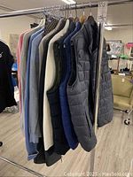 Side view of various men's sweaters, outerwear vests, and pants hanging on rack showing colors and textures