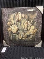 Full view of the unframed 'Pewter Tulips' canvas painting resting upright, showing edges with corner protectors and a textured decorative border around the floral subject.