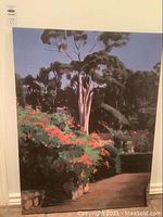 Full view of the unframed landscape painting depicting a tree and orange flowering bushes on canvas.