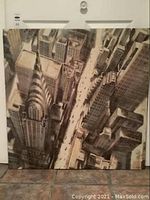 Front view of the unframed canvas artwork showing a cityscape with a tall Chrysler-like building, streets, and surrounding buildings from a bird's-eye perspective.