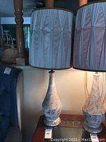 View of lamp with light pink pleated satin fabric lampshade and beige speckled base next to another lamp