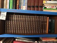 Shelf showing full brown hardcover set of The Book of Knowledge volumes with gold embossed titles plus three additional darker hardcover annual addition volumes on the far right side.