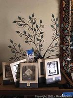 Family tree photo holder shown with multiple attached photo frames holding various photos, details of the leaf-shaped designs on the tree branches are visible.