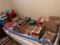 Overview of assorted boxes and packages of vintage Christmas decorations and accessories on a bed.