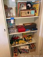 Overview of lot contents on white cabinet shelf: View-Master viewer, records, books, suitcase record player, toy car, Tonka trucks, bag of markers
