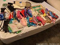Wide assortment of scarves and gloves spread out on a bed, showing various colors, patterns, and fabric types. Includes multiple gloves mostly black or white, several patterned and solid-colored scarves.