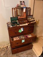 Wooden three-drawer chest topped with jewelry boxes and armoire, top drawer open showing bracelets