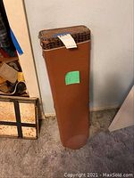 Closed brown rectangular hard case with a label on top, showing wear on the top edge