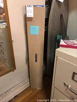 Full view of the long beige textured hard case packaging for the knitting machine, marked with seller and measurements.