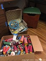 Large cardboard box filled with assorted thread spools in multiple bright colors