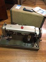 Vintage Universal Super Zigzag sewing machine and hard carrying case on wooden floor.
