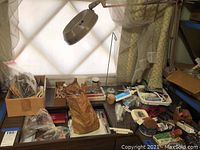 Photo of the seamstress tools spread over a table including various pins, clothespins, spools of thread, and the magnifying swing light attached near the window.