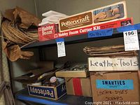 Shelf with leather supplies, pottery wheel kit box, and stacked foam sheets
