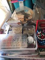 Plastic containers filled with various beads and other crafting supplies, some packaged clever clasps, and crafting tools visible.