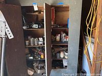 Wide view of open metal cabinet containing various tools and hardware including power tools, jars, and boxes.