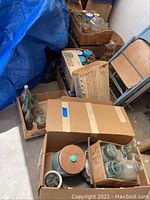 Overall photo showing boxes with Mason jars and assorted glass bottles inside a room with blue tarp and chairs nearby