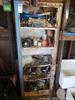 Full view of rusty metal shelf filled with various bolts, nuts, metal parts, and containers containing hardware items