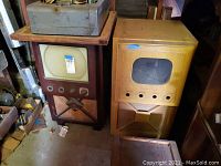 Two vintage TV cabinets side by side on floor, one dark wood with CRT screen and decorative grille, the other yellow with screened front panel and control knobs.