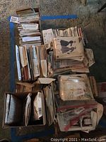 Photo showing a wide view of numerous stacks of vintage sewing patterns, separated into different groupings with some in boxes and others loose. Patterns are paper envelopes with graphics depicting various garments.