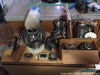 KitchenAid Hobart stand mixer with bowl and various attachments and kitchen tools spread out on countertop and in cardboard boxes.