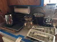 Photo showing various kitchen items including a coffee pot, warming tray, ice bucket, carafe, vintage blender, and three aluminum ice cube trays