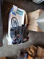 Full view of Dirt Devil vacuum sitting on a box, showing wear and cord loosely coiled next to it