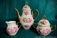 Coffee pot with lid, sugar bowl with lid and creamer arranged against green backdrop