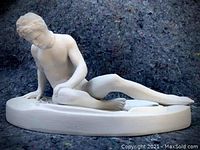Front angled view of the white alabaster figurine statue depicting a nude male figure seated semi-reclining on an oval base.