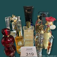 Overall group shot showing red curvy bottle, gold floral bottle, frosted square bottle, black tube, gold lattice bottle and novelty doll container