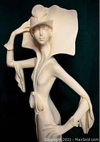 Front and side view of the tall Art Deco lady figurine in an elegant pose with a wide brim hat and flowing dress on a wooden base.