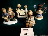 Photo of the four Hummel figurines arranged on a dark surface, showing Drumming for Joy, Happy Pastime, Little Cocopah Indian Girl, and Wishes Come True BH17.