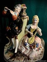 Porcelain statue showing the man with flute on left and woman with lute on right beneath a decorative floral backdrop