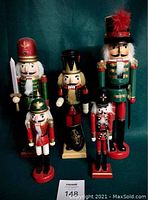 Photo showing all five nutcracker figurines of various sizes dressed in holiday attire against green background.