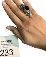 Chunky ornate silver ring with central black onyx stone and turquoise stones on either side worn on finger, showing its size and fit.