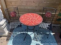 Full view showing round mosaic tile table with red circular pattern and two wrought iron chairs with matching mosaic backs