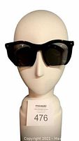 Front view of the sunglasses displayed on a white head mannequin showing the round black acetate frames and dark lenses.