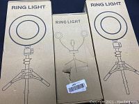 Boxed ring lights showing line art of ring light and tripod stand. Three boxes shown: two with one ring light, one with dual light design.